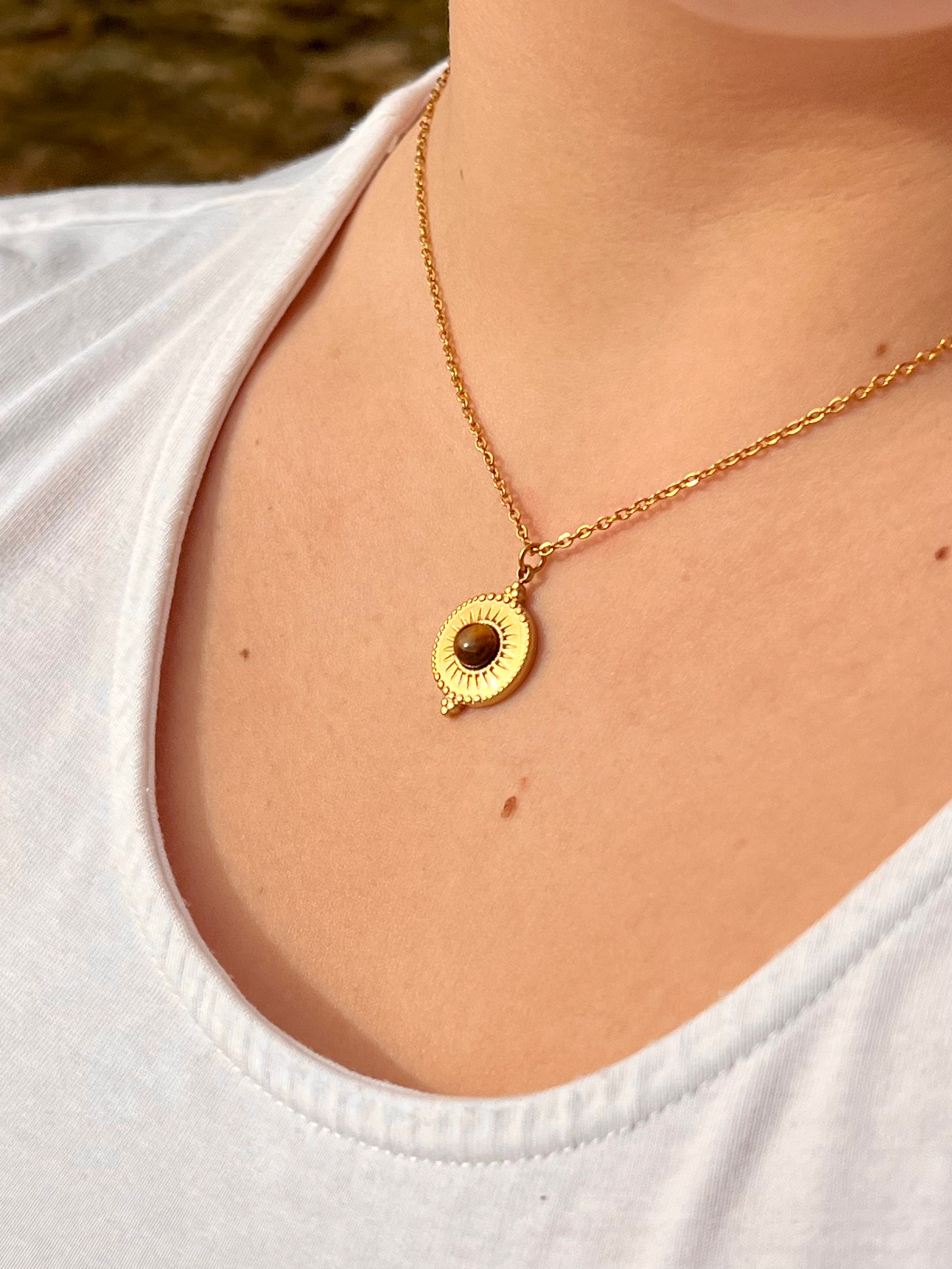 Collier ZÉLIE en acier inoxydable doré et pierre d'oeil de tigre, porté par une fille dans les rochers